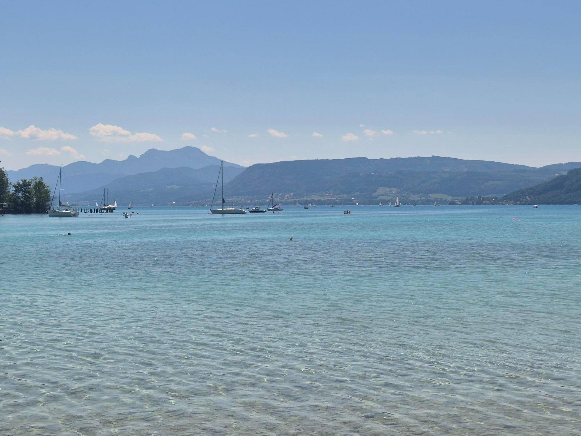 Klares, türkisfarbenes Seewasser mit Booten und einer malerischen Bergkulisse am Horizont.