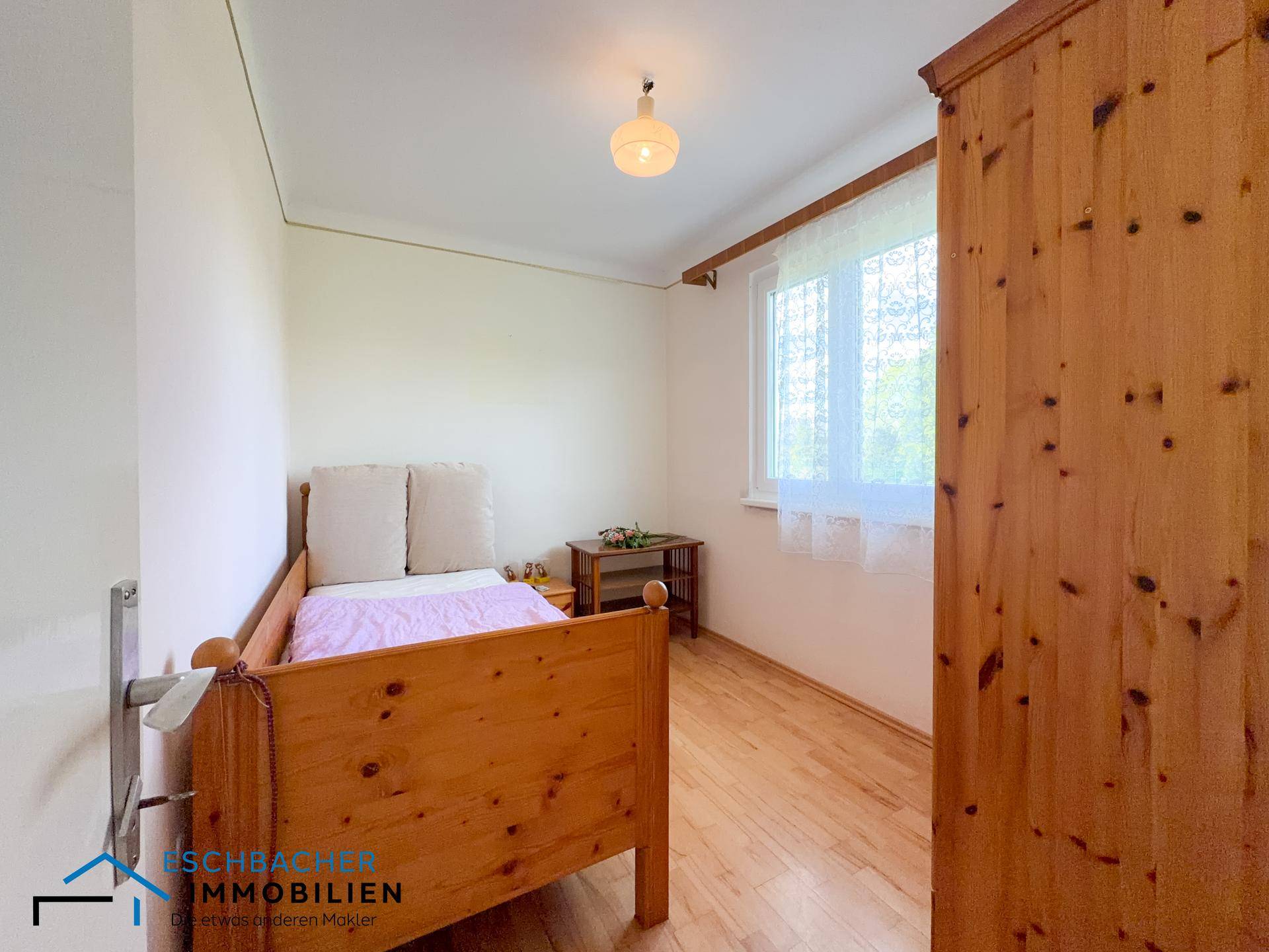 Helles Schlafzimmer mit Einzelbett, Holzschrank und Fenster mit Blick ins Grüne.