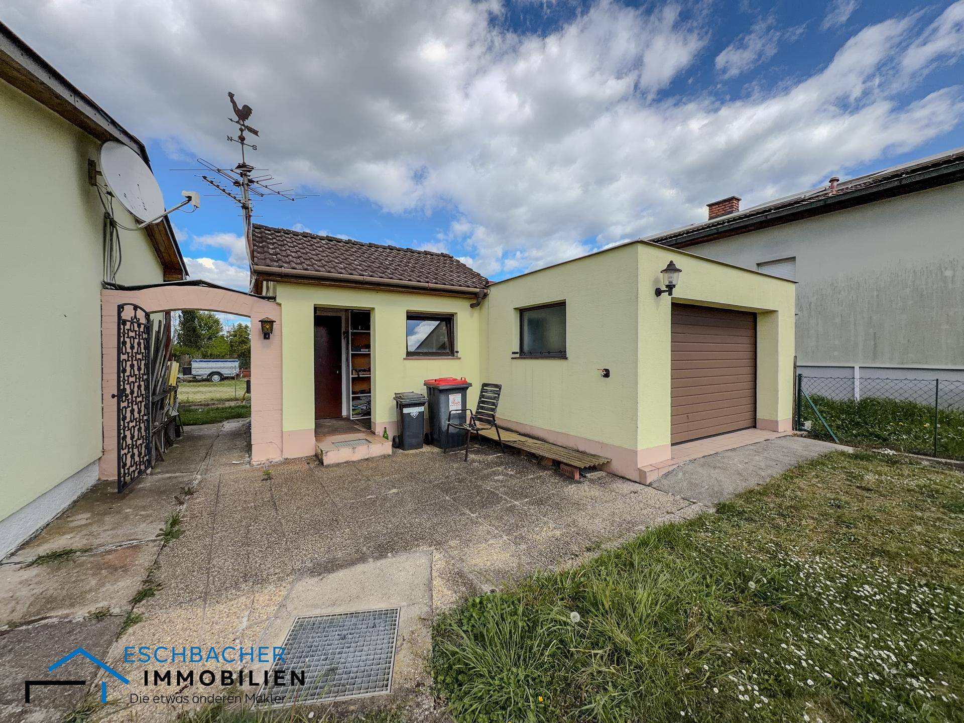Seitenansicht des Hauses mit Garage und einem kleinen gepflasterten Bereich neben dem Eingang.