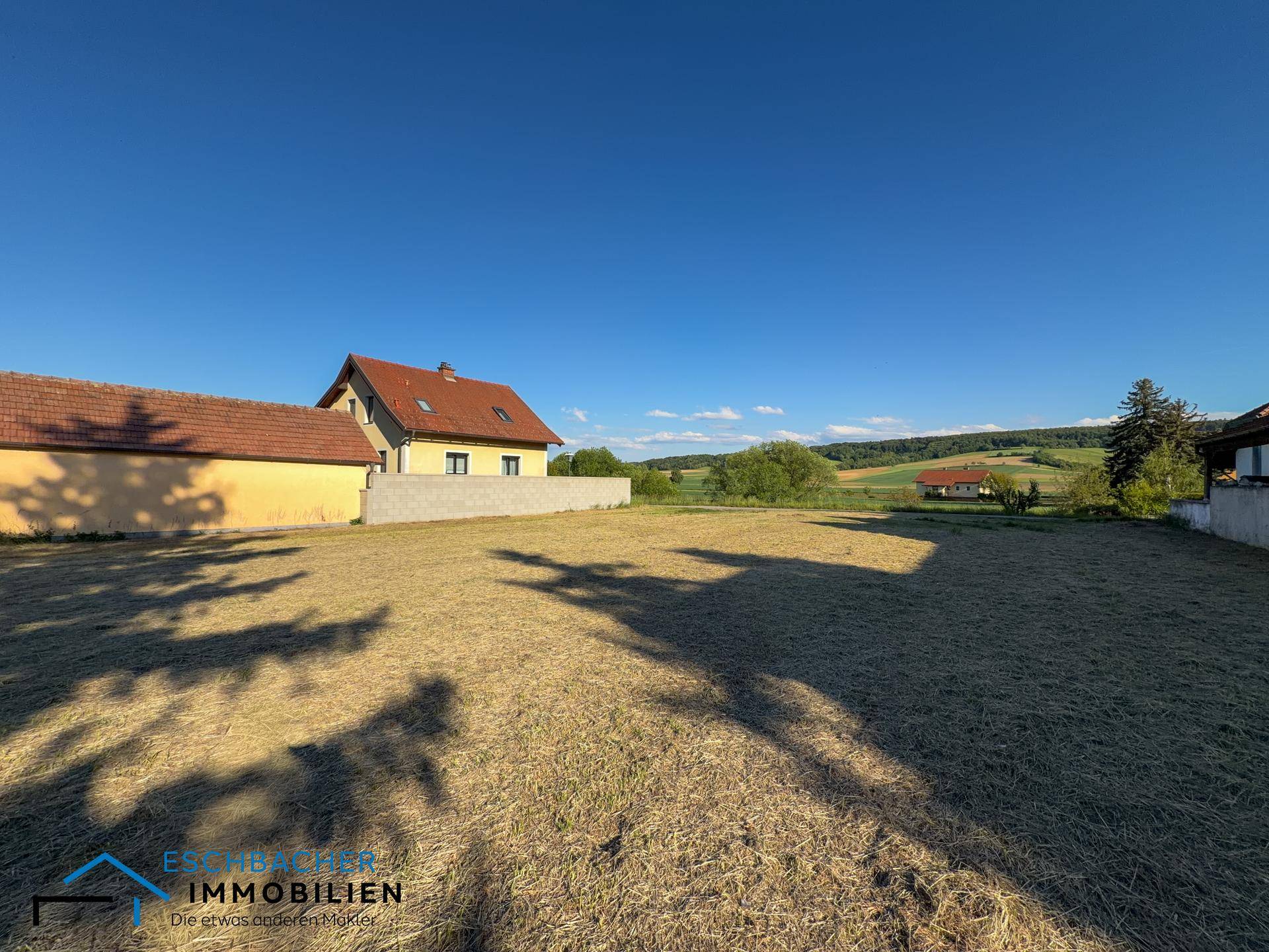 Weitläufiges Grundstück mit gemähtem Gras und Wohnhäusern im Hintergrund unter klarem Himmel.
