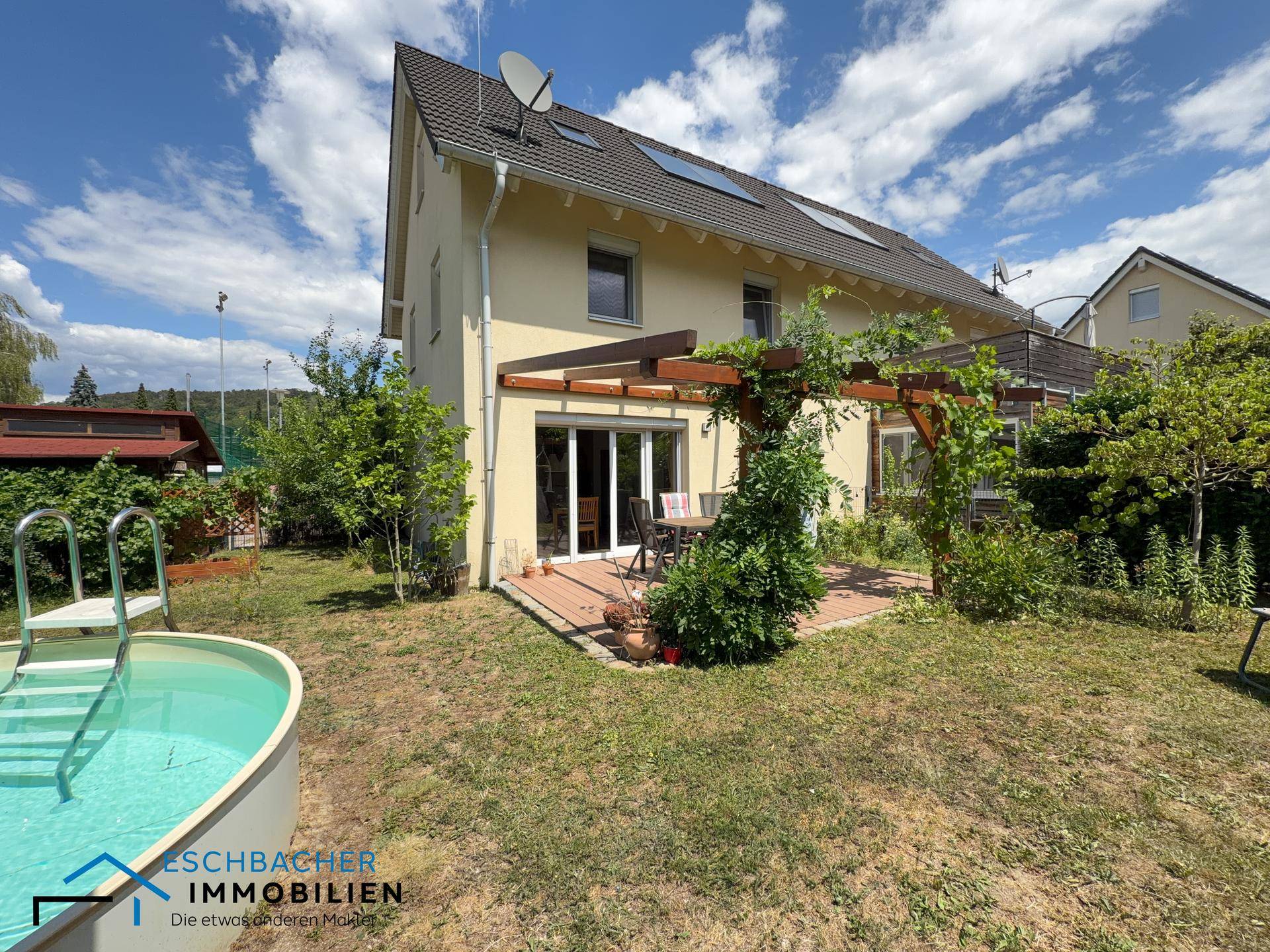 Rückansicht des Hauses mit Terrasse, Garten und einem kleinen Aufstellpool unter blauem Himmel.