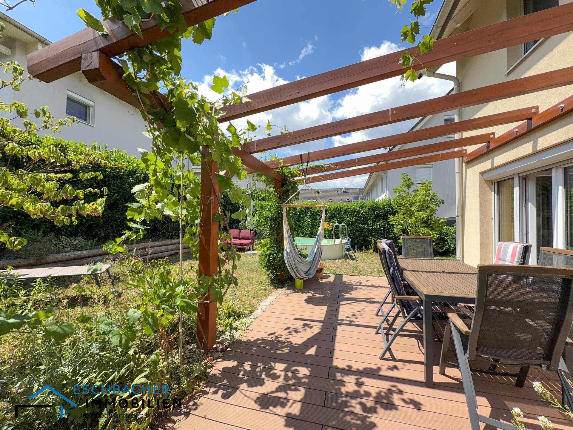 Sonniger Terrassenbereich mit Holzpergola, Hängematte und Blick auf den Garten mit Pool.