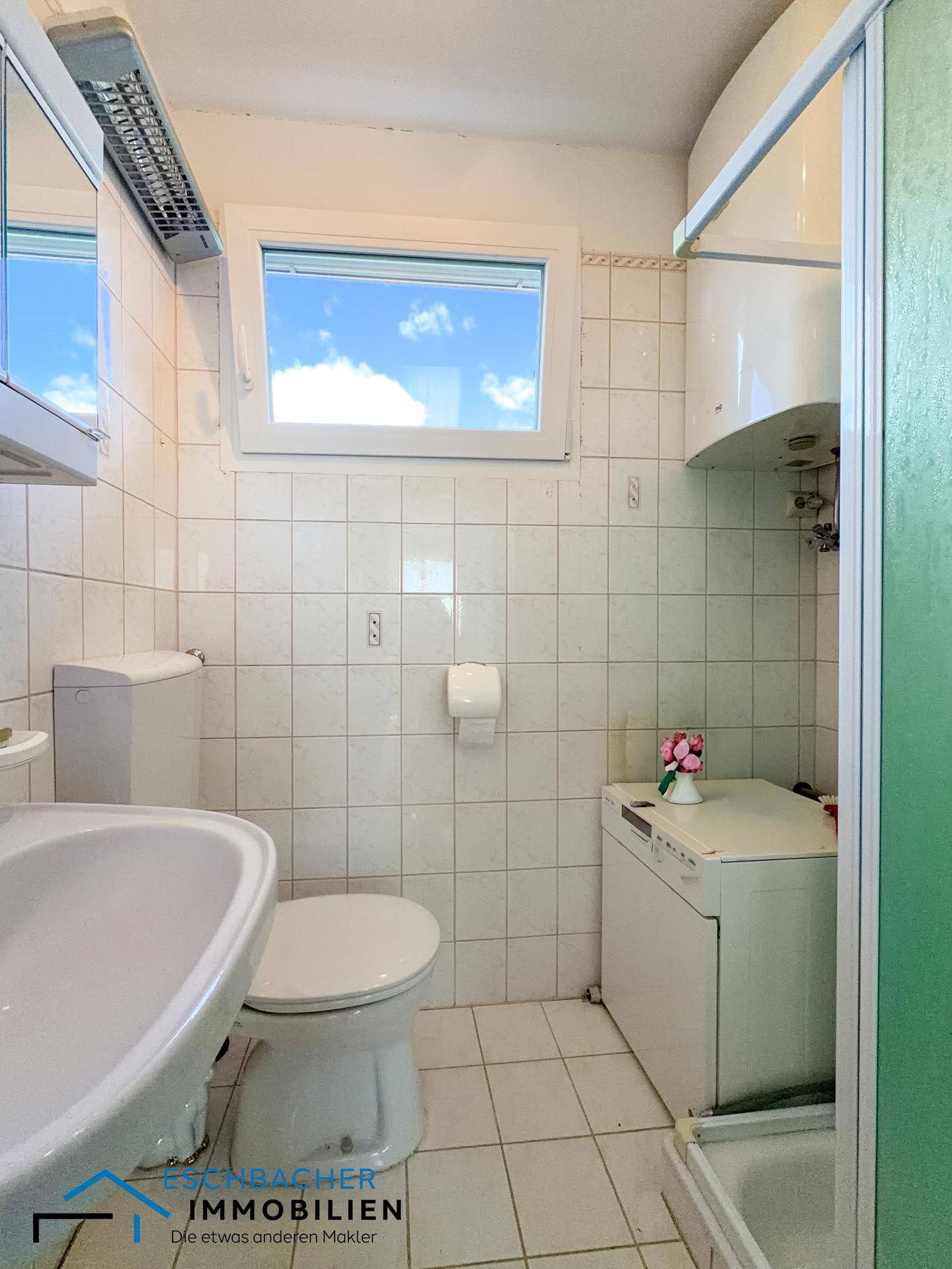 Gefliestes Badezimmer mit WC, Waschbecken, Dusche und Fenster für Tageslicht.