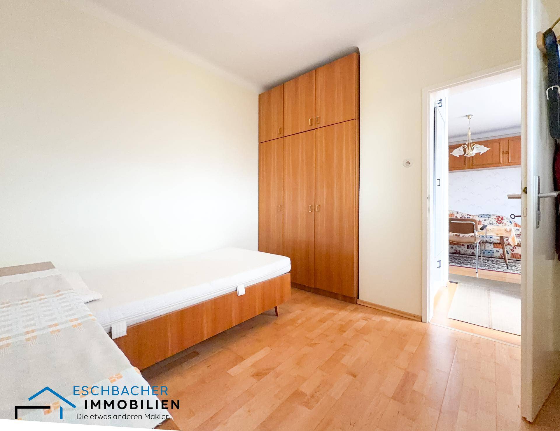 Schlafzimmer mit Einzelbett, großem Holzschrank und Blick in den Flur.