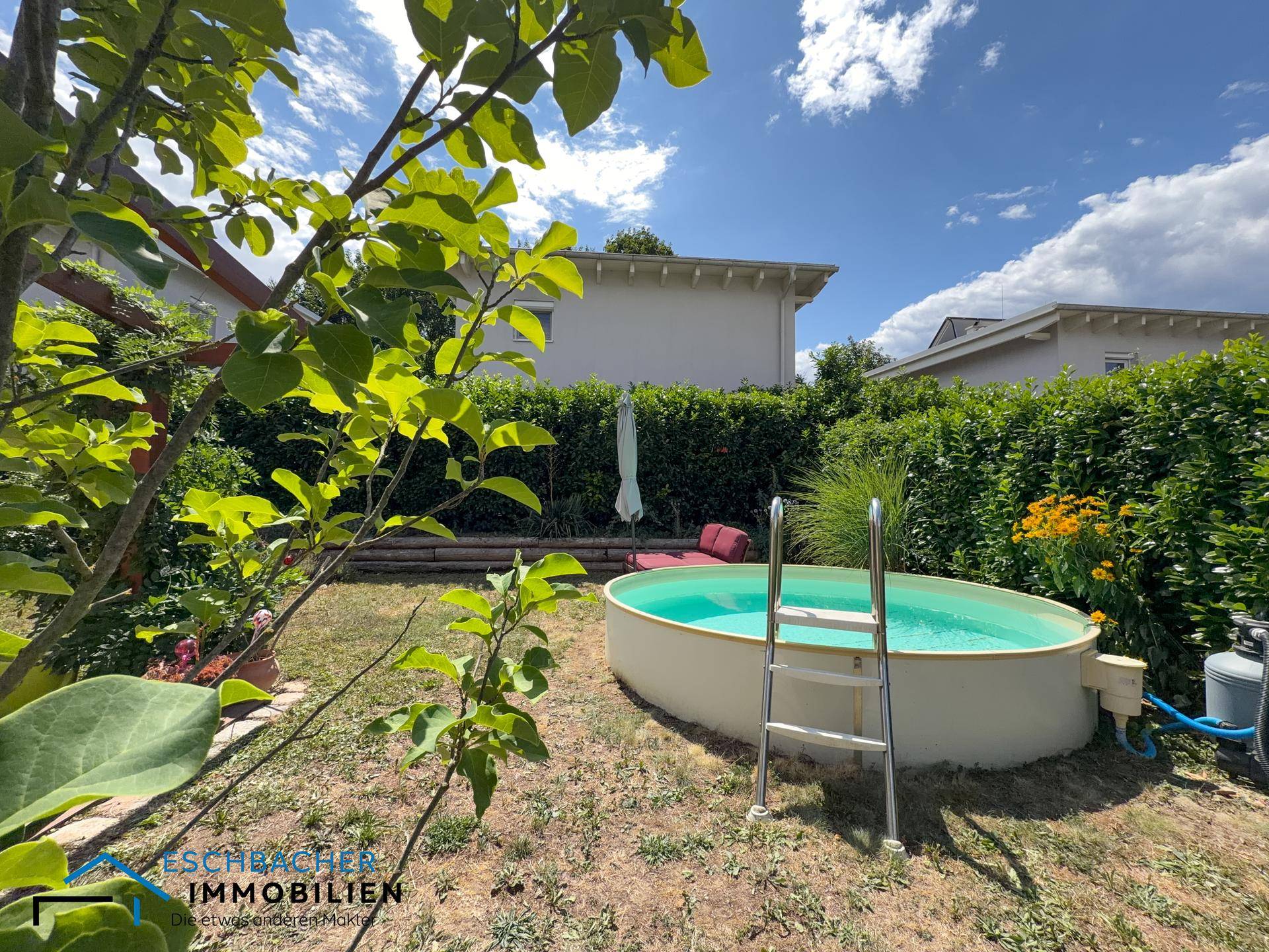 Garten mit Aufstellpool, umgeben von üppigem Grün und blühenden Pflanzen.