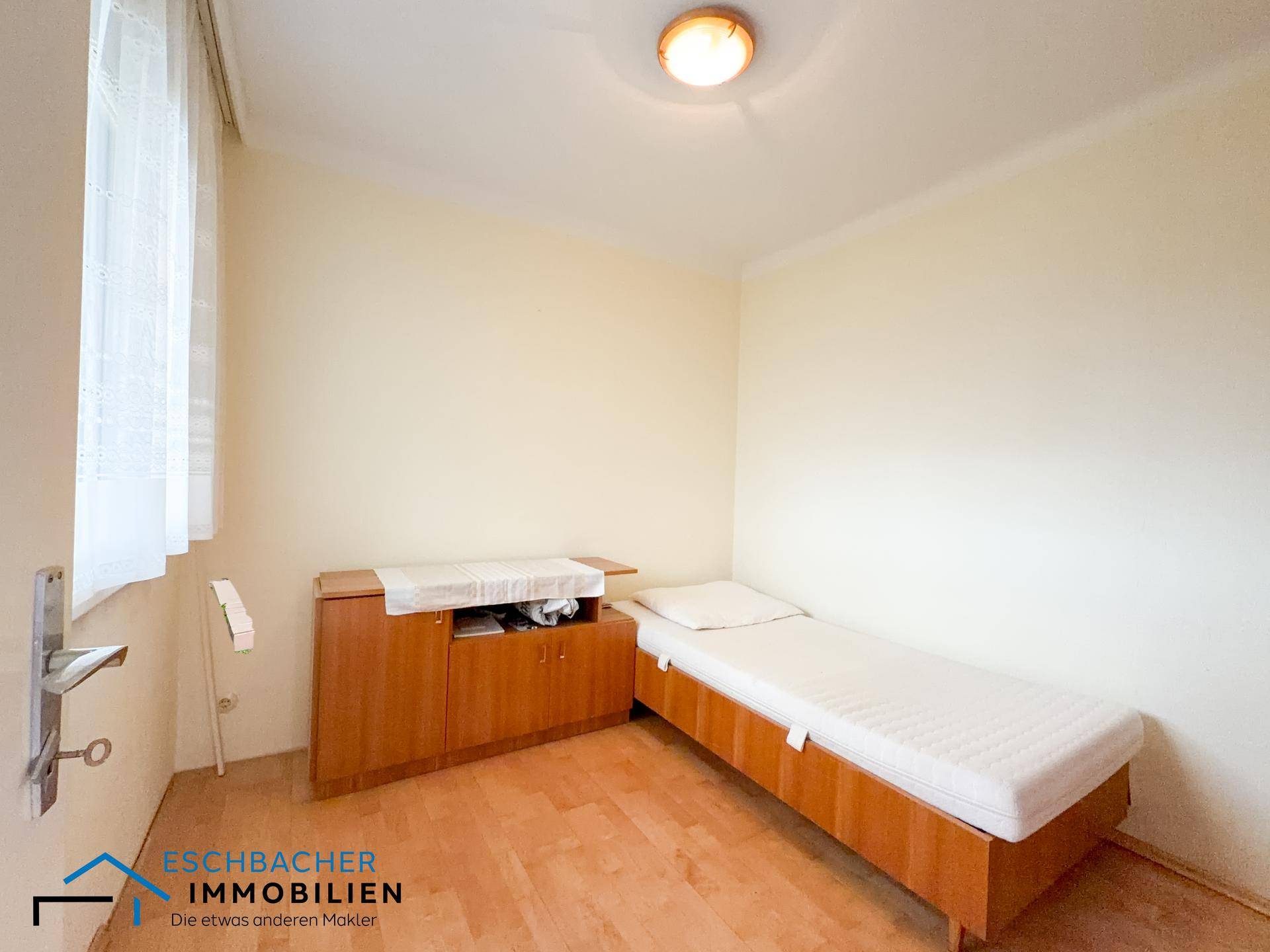 Helles Schlafzimmer mit Einzelbett, Holzmöbeln und Parkettboden.