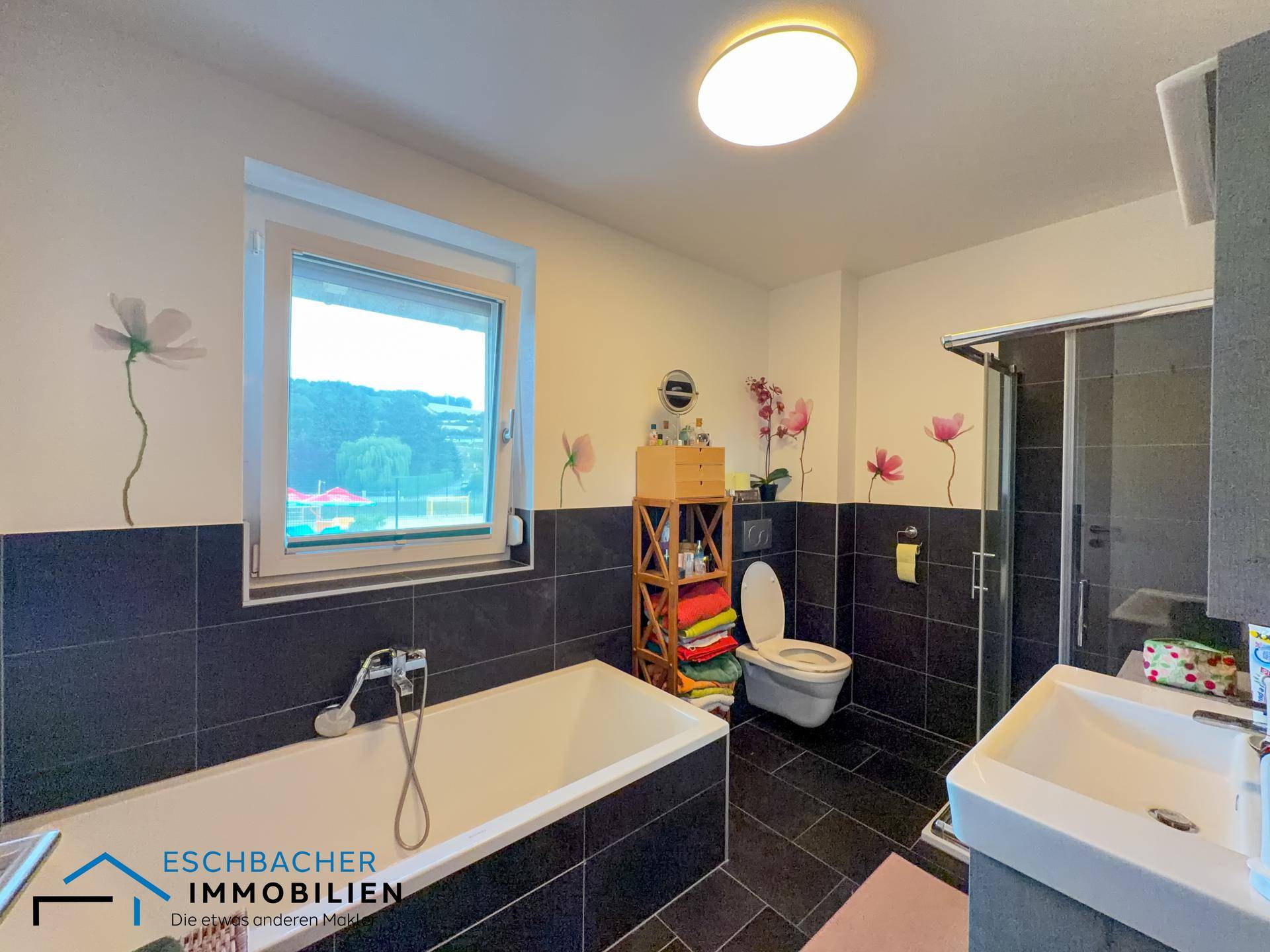 Helles Badezimmer mit Badewanne, Dusche, WC und Fenster mit Blick ins Grüne.