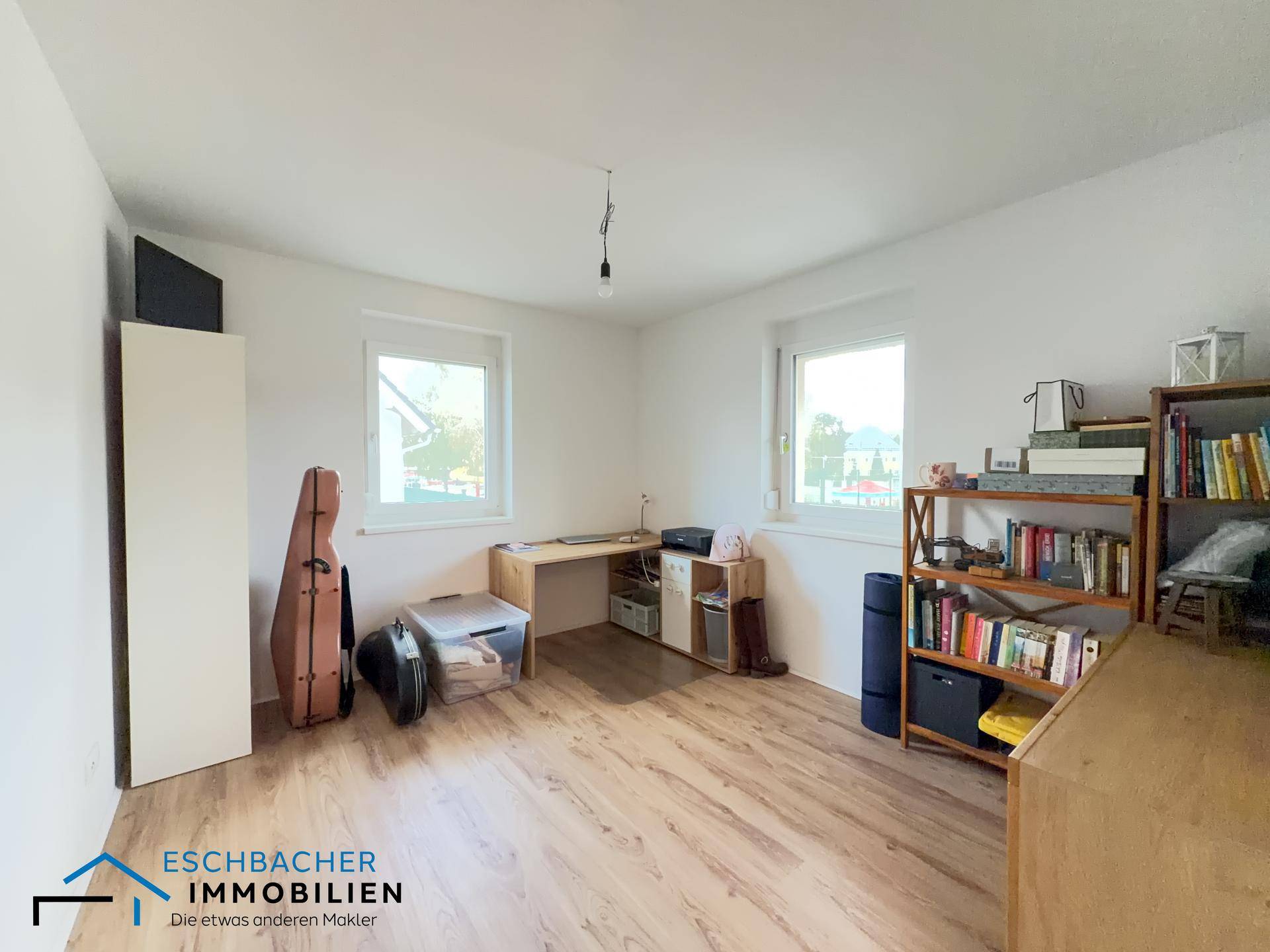 Helles Zimmer mit Holzfußboden, Schreibtisch und Bücherregal, ideal als Büro nutzbar.