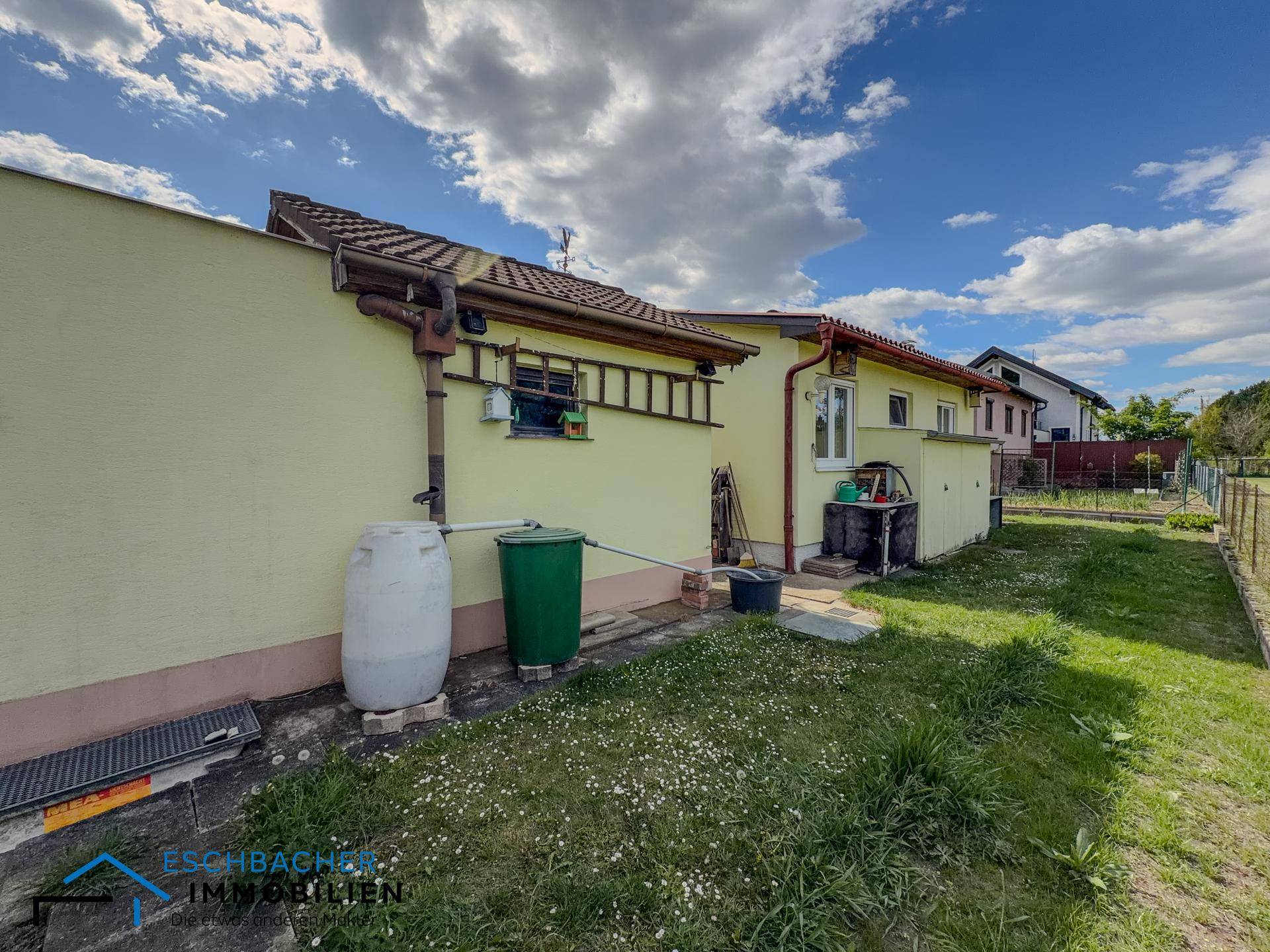 Rückseite des Hauses mit Regenwassertonnen und einem kleinen Gartenbereich.