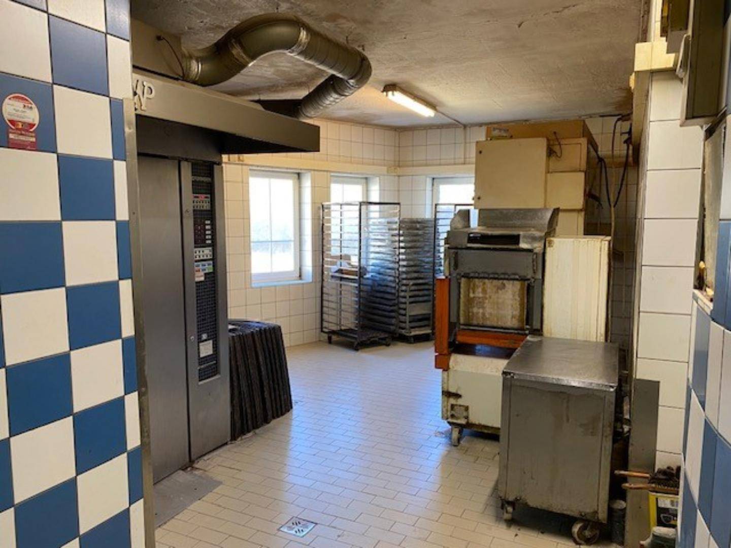 Geräumiger Produktionsbereich einer Bäckerei mit großen Öfen, Backblechwagen und Fenstern für Tageslicht.