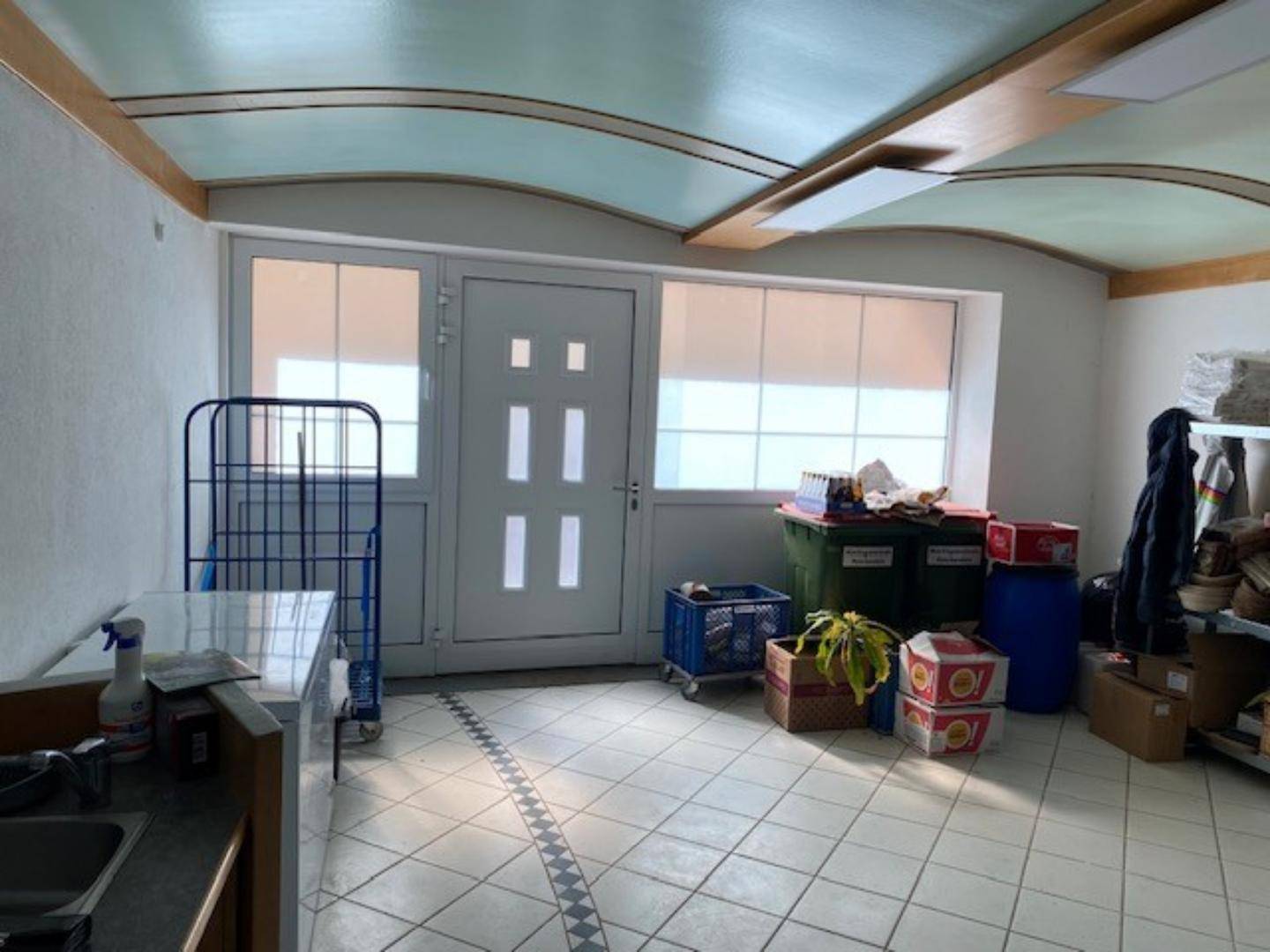 Lagerraum mit großen Fenstern und einer Tür, Fliesenboden und einer dekorativen Decke, genutzt für verschiedene Lagergüter.