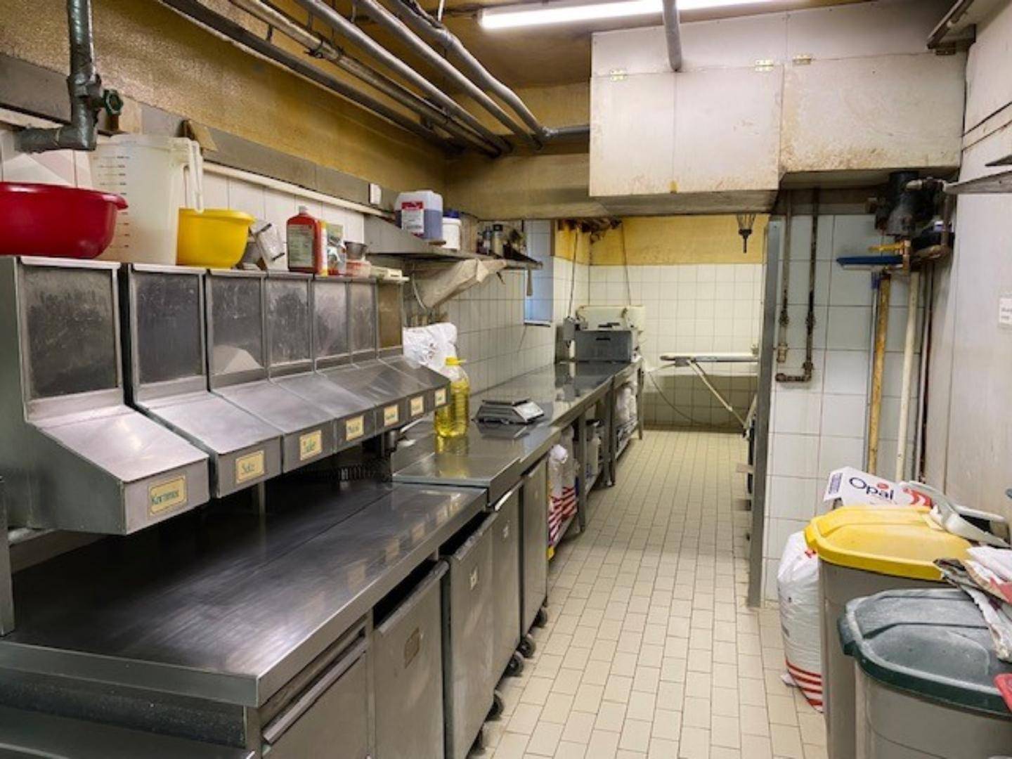 Funktionale Industrieküche mit langen Edelstahlarbeitsflächen, Fliesenwänden und praktischen Lagerbehältern für den Betrieb.