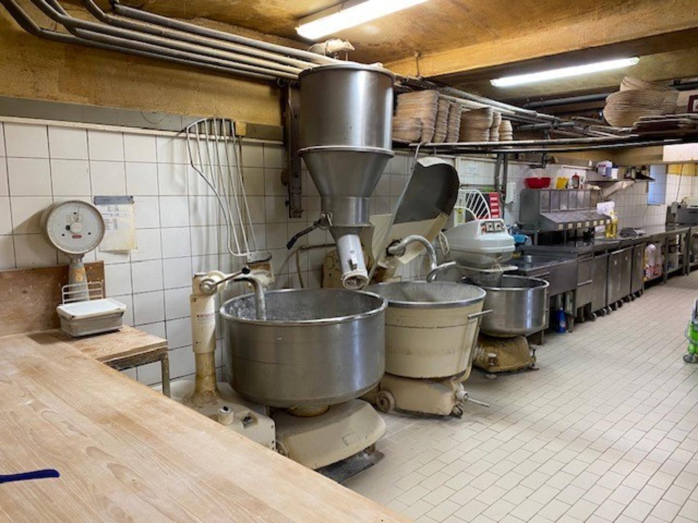 Detailansicht der Bäckereiküche mit großen Teigmischern, einer alten Waage und einer robusten Holzarbeitsplatte.