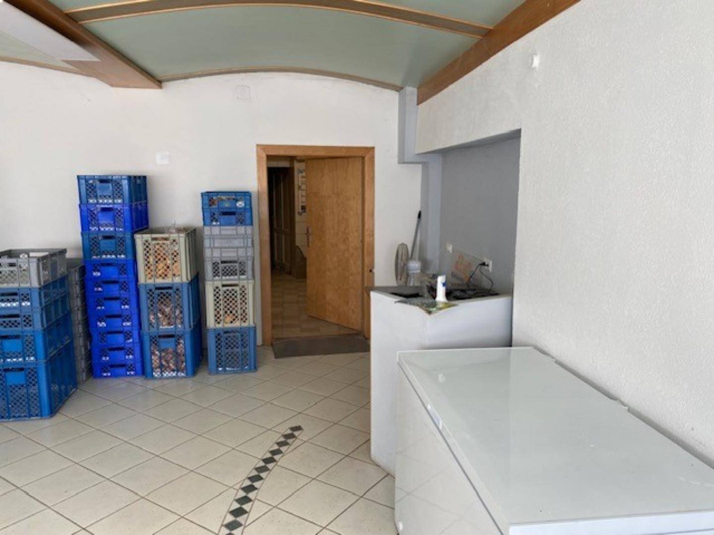 Lagerraum mit gestapelten Kisten, einem Gefrierschrank und einem Durchgang, gekennzeichnet durch Fliesenboden und eine dekorative Decke.