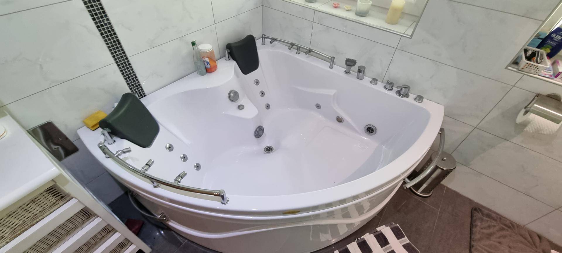 Modernes Badezimmer mit großer Eck-Whirlpool-Badewanne und Fliesen an den Wänden.