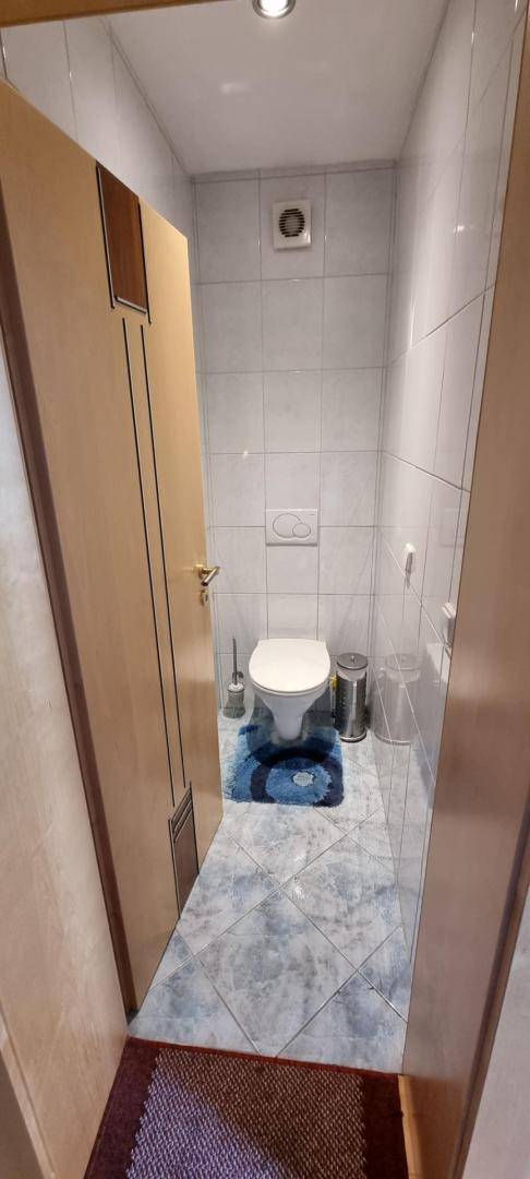 Kleines Gäste-WC mit hellen Fliesen und wandmontierter Toilette.
