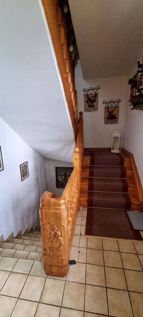 Holztreppe mit kunstvoll geschnitztem Geländer und Fliesenboden im Eingangsbereich.