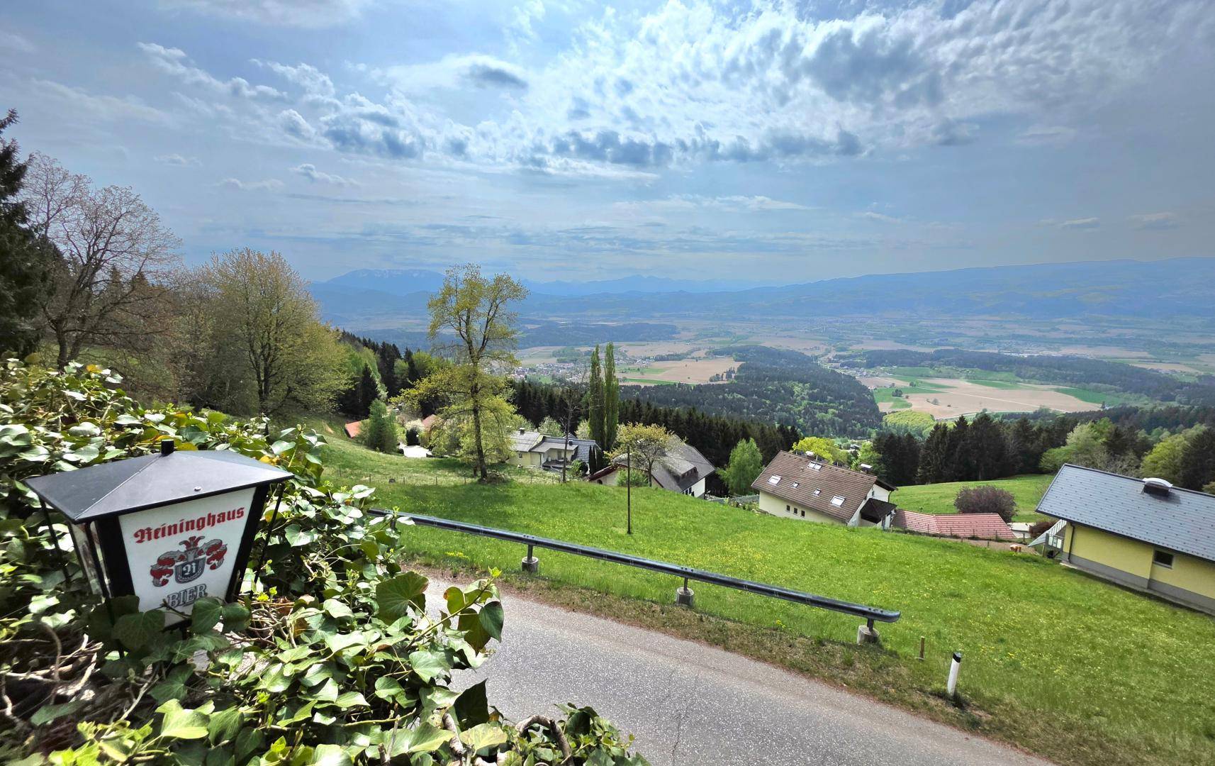 Weitläufige grüne Landschaft mit Häusern und einem Hinweisschild unter bewölktem Himmel.