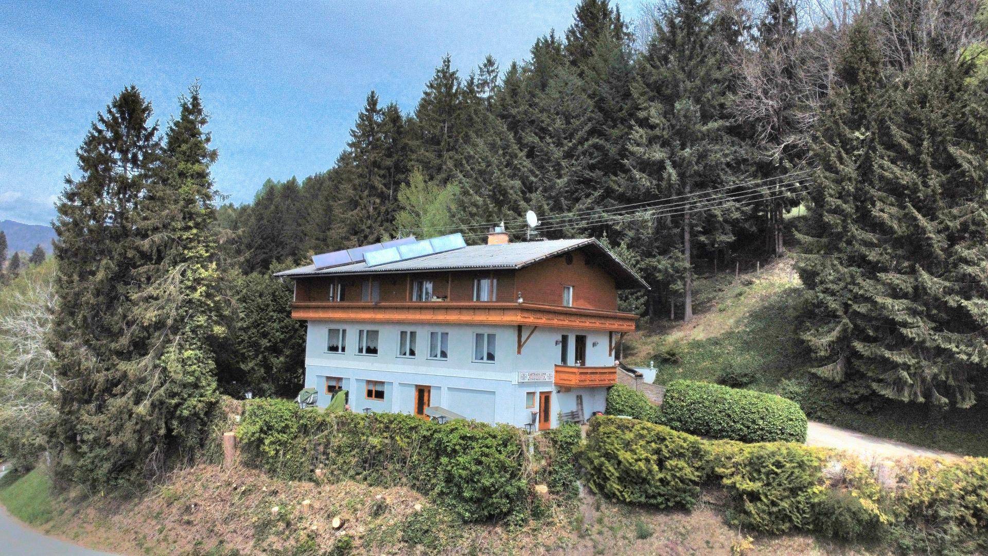 Mehrstöckiges Gebäude in ländlicher Umgebung, umgeben von hohen Bäumen und viel Grün.