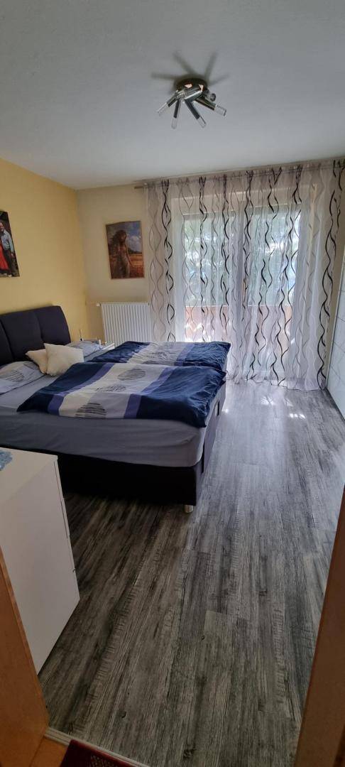 Schlafzimmer mit modernem Laminatboden, Doppelbett und großen Fenstern mit Vorhängen.