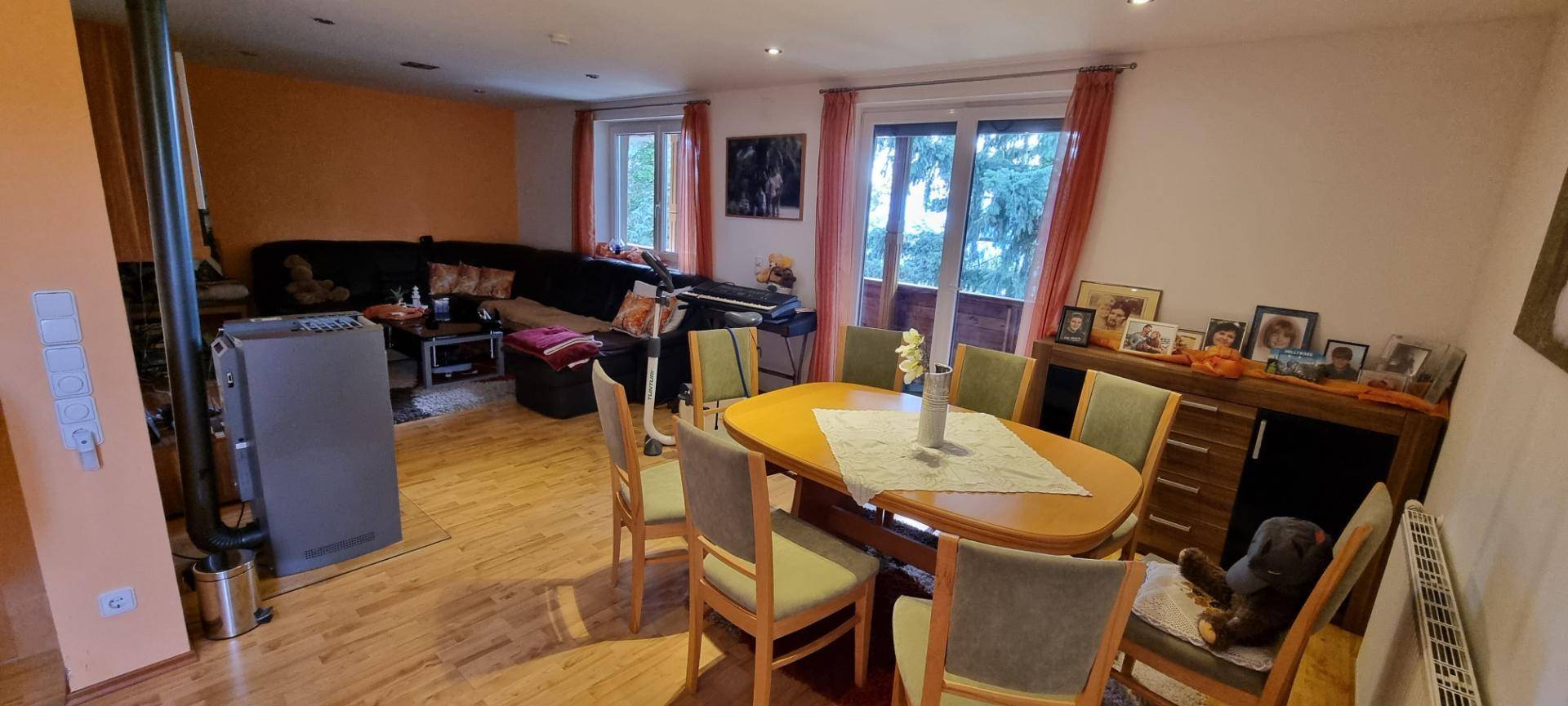 Geräumiger Wohn-Essbereich mit Holzboden, Kaminofen und Zugang zum Balkon.