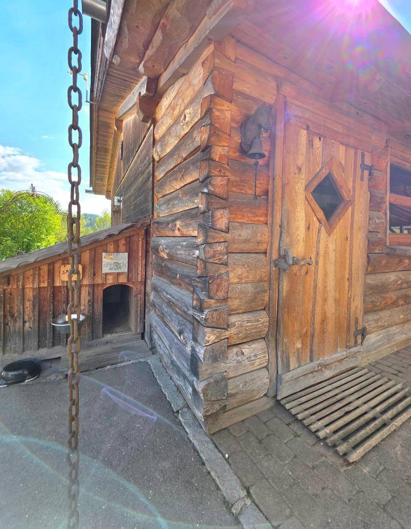 Rustikale Holzfassade eines Nebengebäudes mit einem kleinen Hundezwinger und einer Kette im Vordergrund.