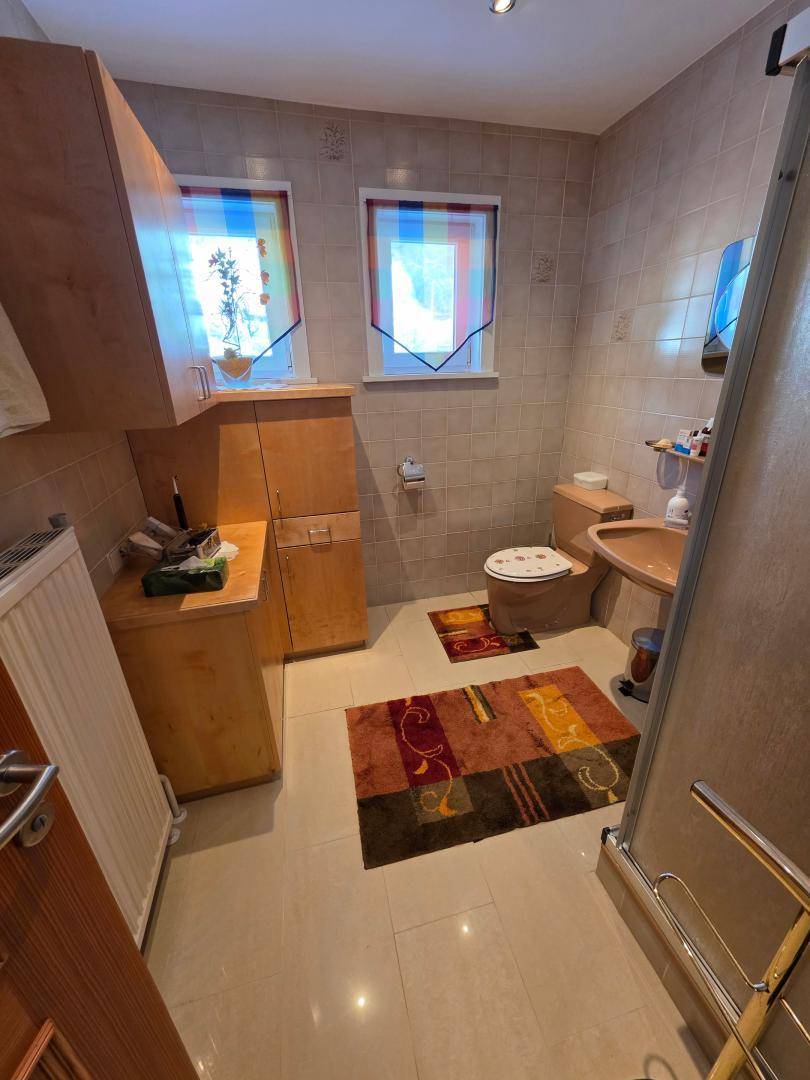 Badezimmer mit beigen Fliesen, einer Dusche und einem Fenster, das für natürliches Licht sorgt.