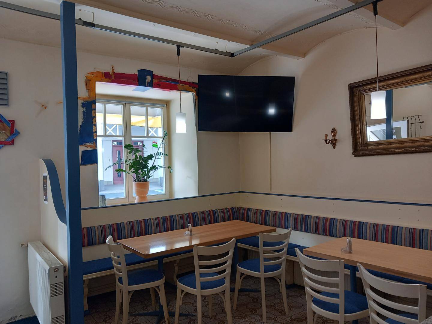 Gemütlicher Sitzbereich mit Wandbank, Tischen, Fernseher und Blick auf einen ruhigen Innenhof.