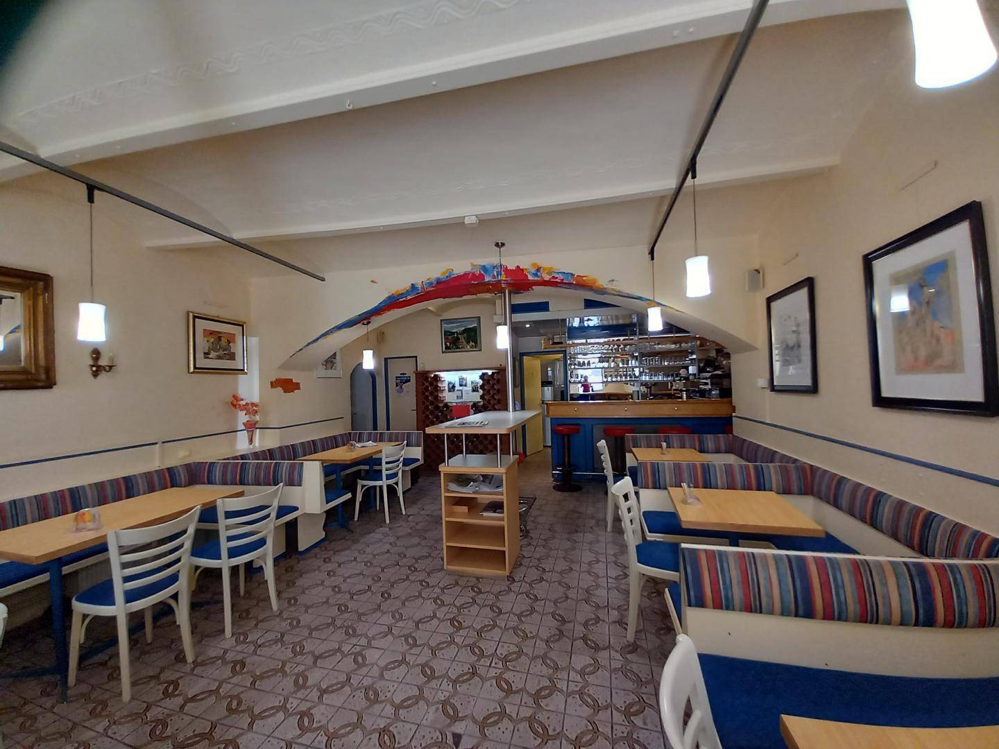 Geräumiger Gastraum eines Cafés mit mehreren Sitzbereichen, einer Bar im Hintergrund und einem gewölbten Deckenbereich.