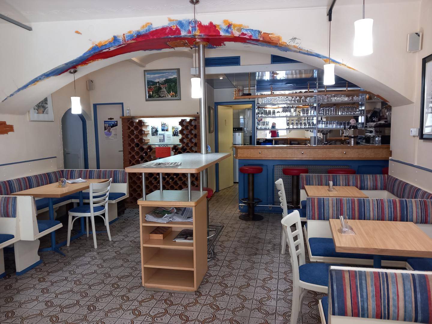 Gemütlicher Gastraum mit Sitzbänken, Holztischen und einer gut ausgestatteten Bar im Hintergrund.