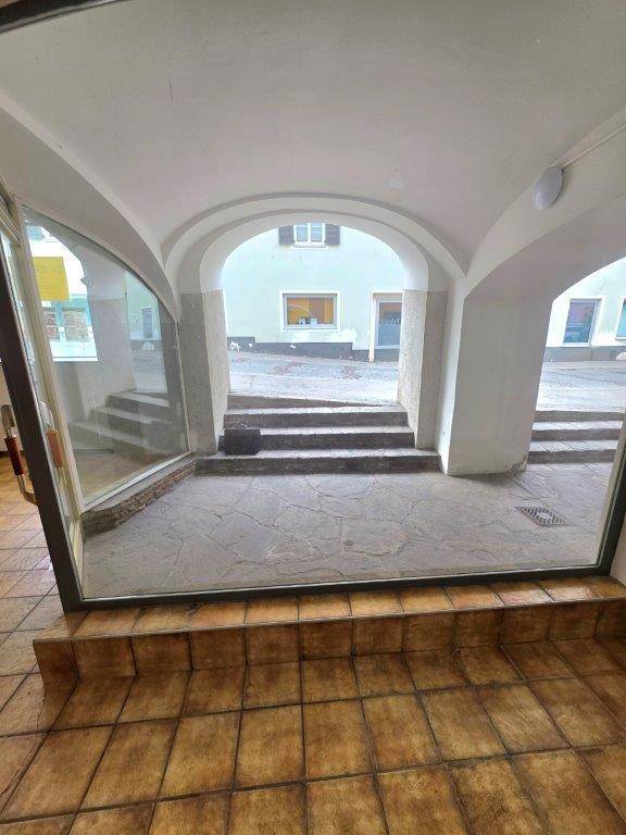 Blick aus dem Innenraum durch eine Glastür auf einen gepflasterten Außenbereich mit Stufen und einem weiteren Gebäude.