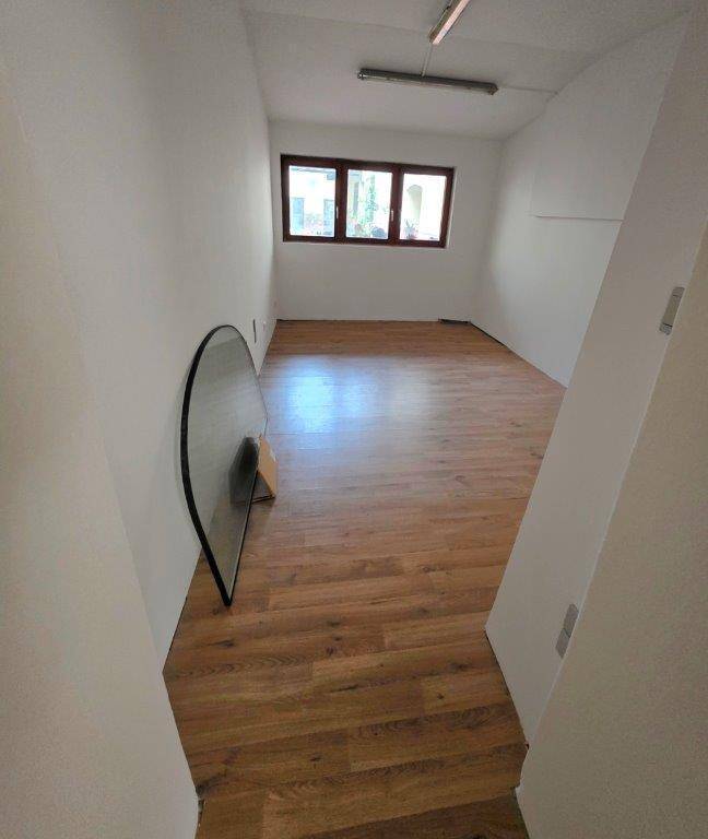 Schlichter Raum mit Holzplankenboden und drei rechteckigen Fenstern, die für ausreichend Tageslicht sorgen.