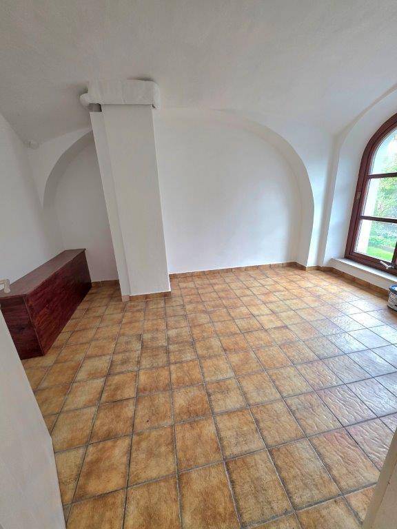 Heller Raum mit Terrakotta-Fliesenboden, hohen Gewölbedecken und einem großen Rundbogenfenster, das viel Licht spendet.
