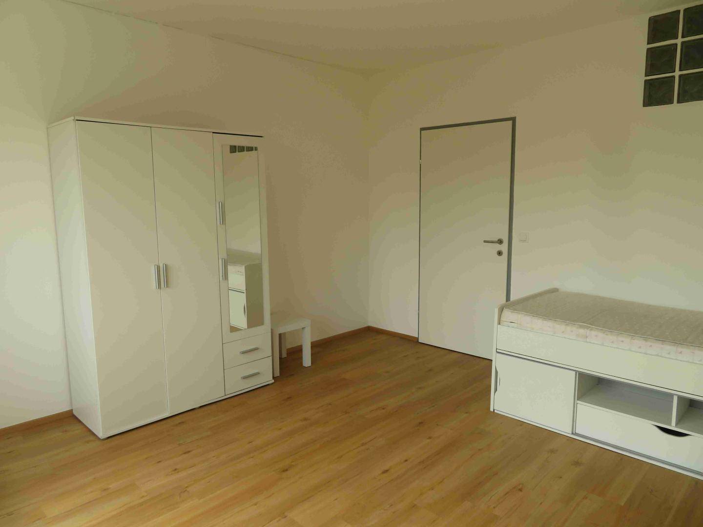Schlafzimmer mit hellem Holzboden und einem weißen Kleiderschrank mit Spiegeltür.