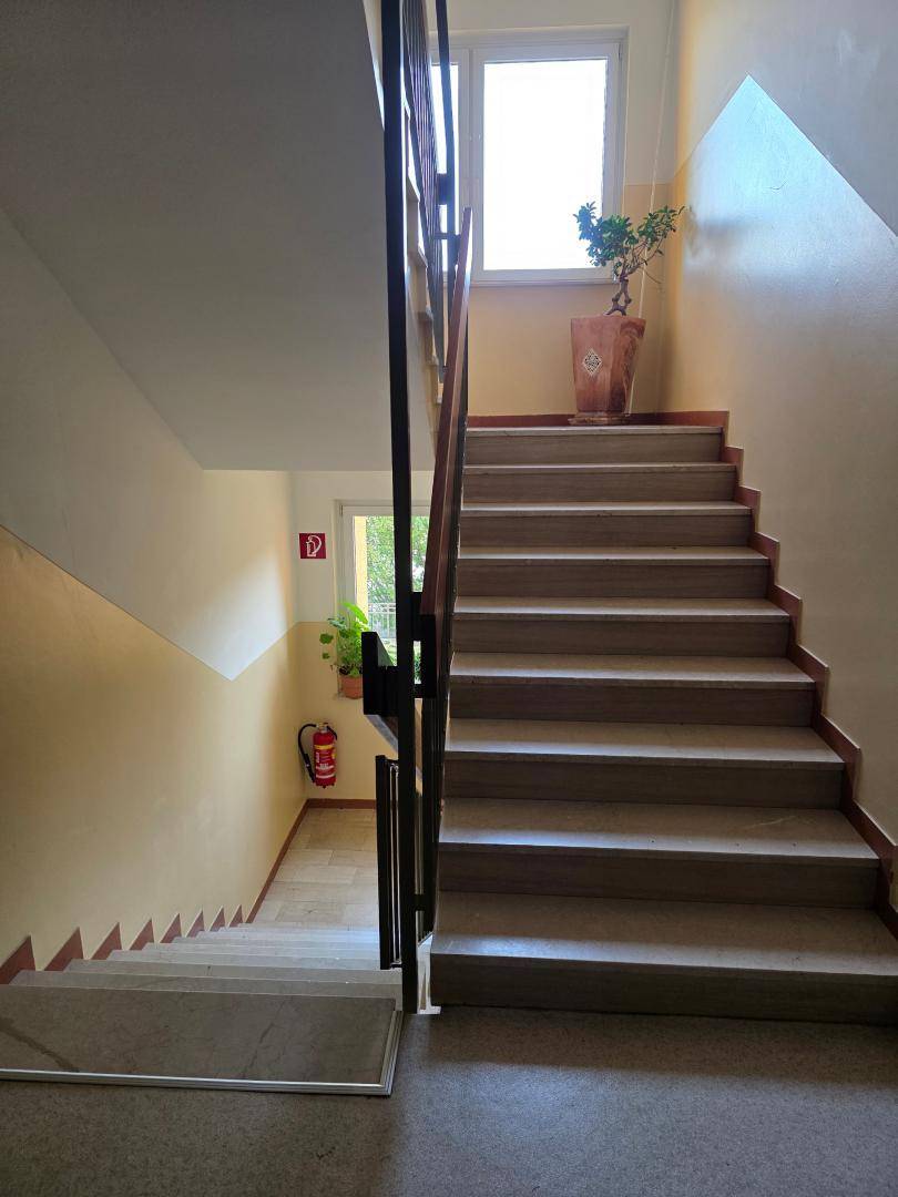 Treppenhaus mit Holzgeländer und Fenstern, die Tageslicht in den Flur lassen.
