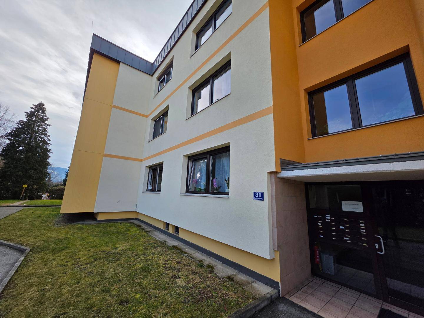 Fassade eines modernen Mehrfamilienhauses mit gelb-orangen Akzenten und Fenstern.