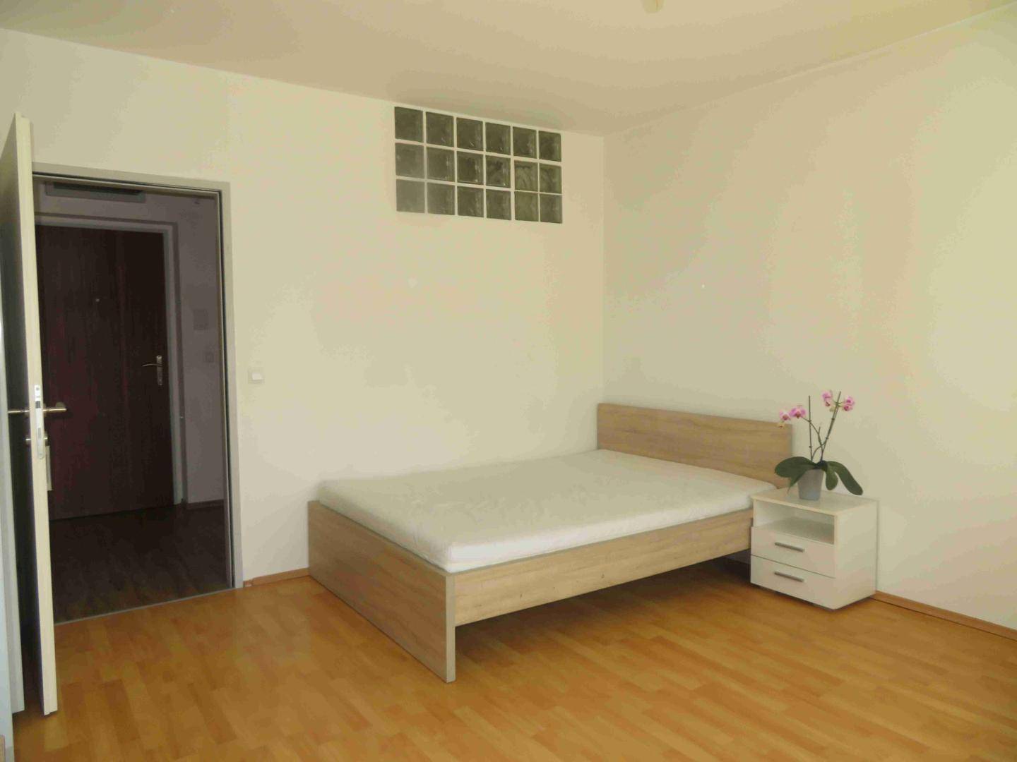 Helles Schlafzimmer mit Holzboden, Bett und Nachttisch, durch eine Tür zugänglich.