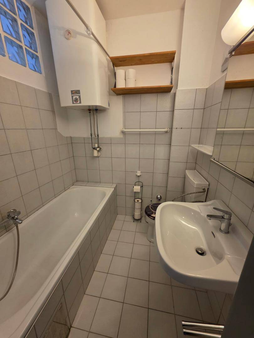 Badezimmer mit Badewanne, Waschbecken und WC, hell gefliest und mit Fenster.