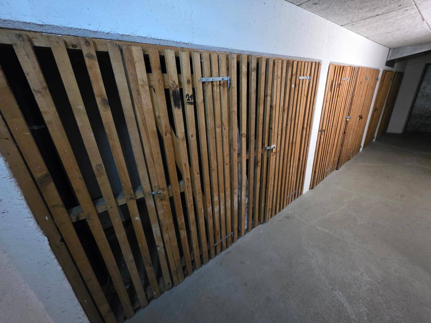 Reihe von individuellen Lagerabteilen aus Holzlatten in einem Kellerbereich.