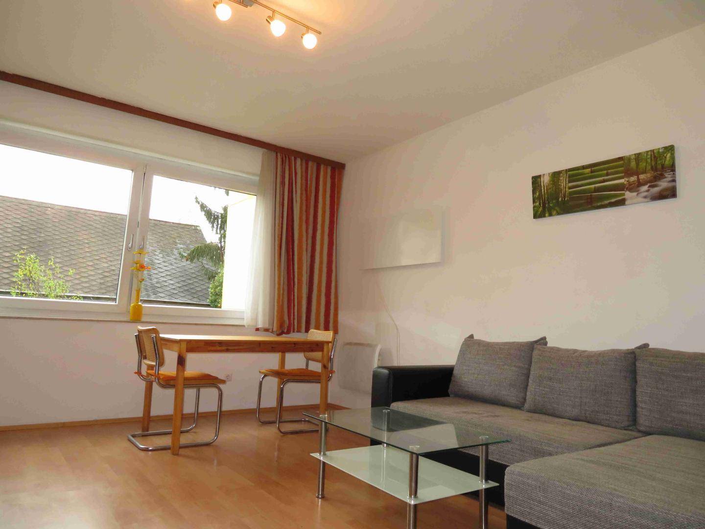 Gemütliches Wohnzimmer mit Sofa, kleinem Esstisch und Blick ins Grüne durch die Fenster.