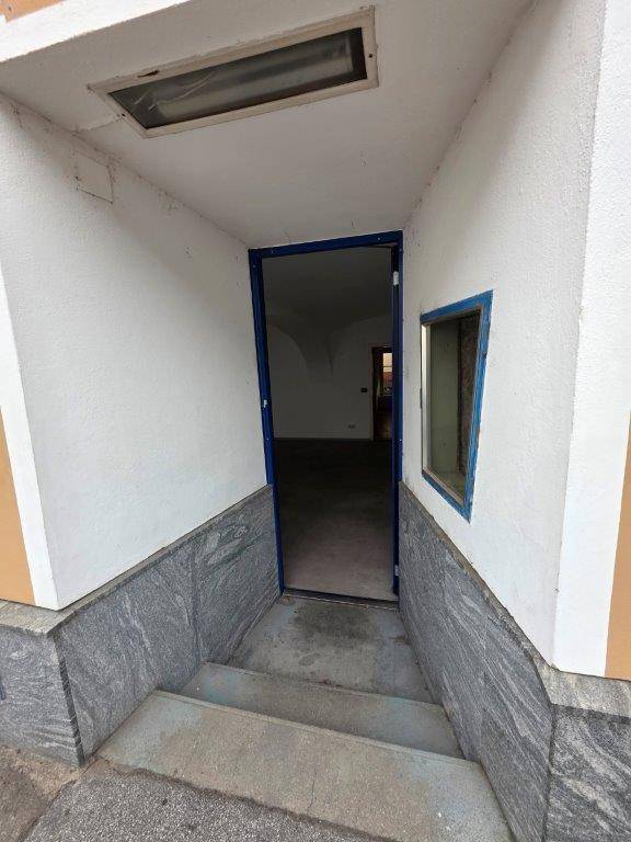 Eingangsbereich mit Treppe, die zu einer blauen Tür führt, umgeben von weißen Wänden und Steinsockel.
