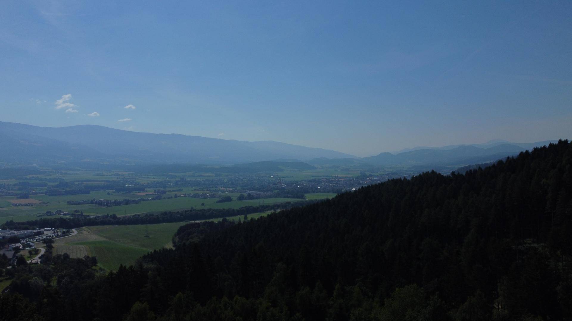Weitläufige Luftaufnahme eines Tals mit Feldern und Wäldern unter klarem blauem Himmel.