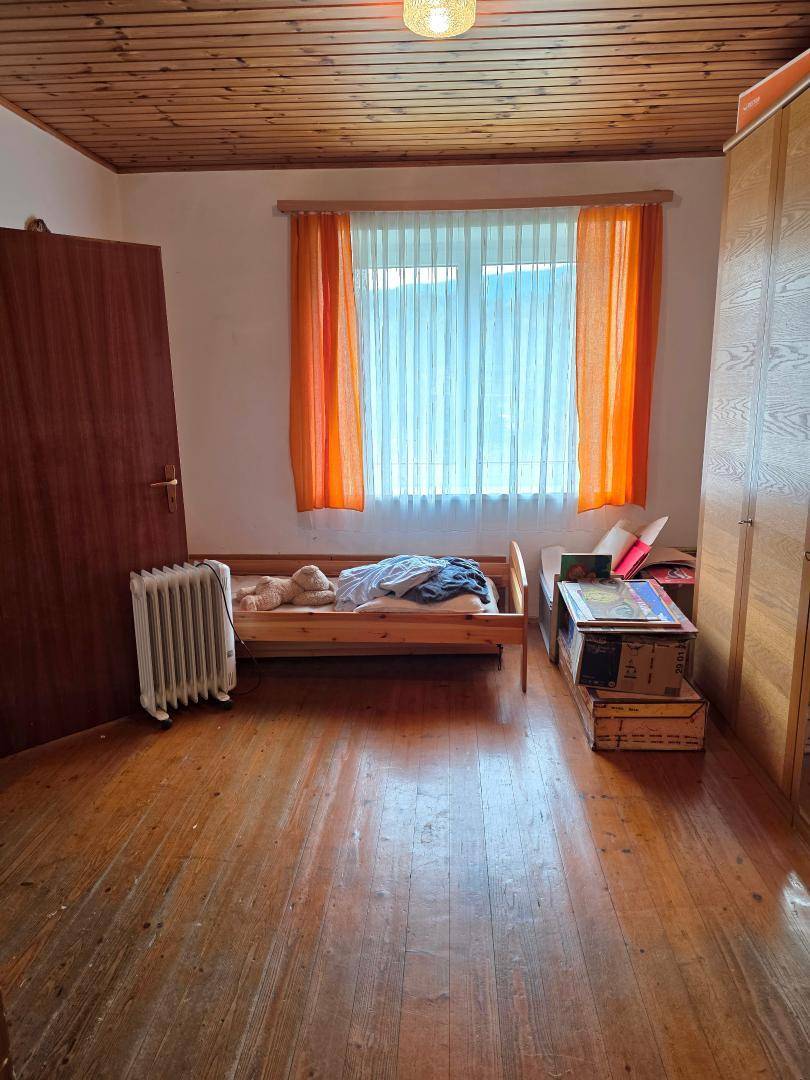 Schlafzimmer mit Einzelbett, Holzdecke und Heizkörper, durch ein Fenster gut beleuchtet.