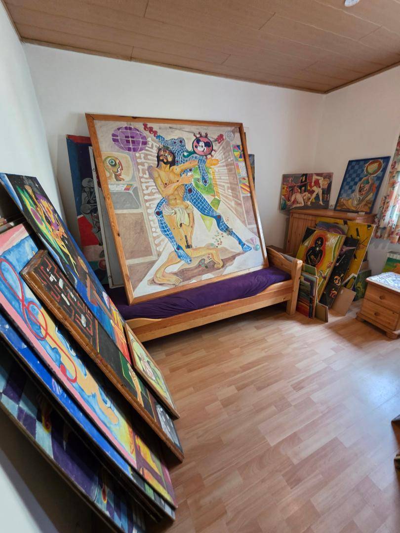 Raum, der als Atelier oder Lager für Kunstwerke genutzt wird, mit einem Bett und Laminatboden.