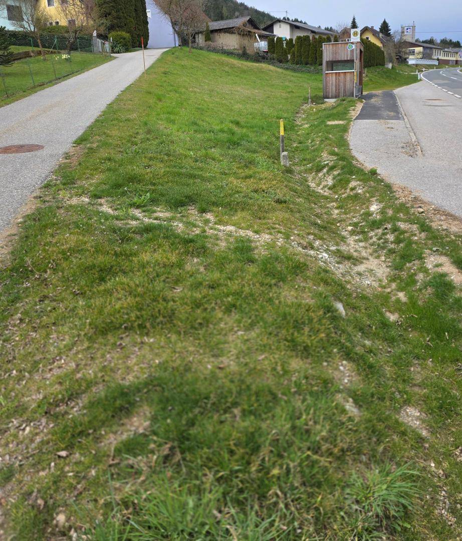 Straßenansicht mit einem grasbewachsenen Hang, einem Weg und Häusern in der Ferne.