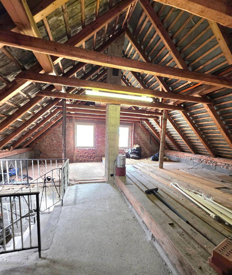 Unausgebauter Dachboden mit sichtbaren Holzbalken und Fenstern, bietet Ausbaupotenzial.