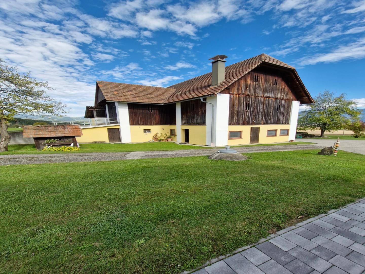 Traditionelles Bauernhaus mit Holzelementen und Ziegeldach, umgeben von grünem Rasen und einem gepflasterten Weg.