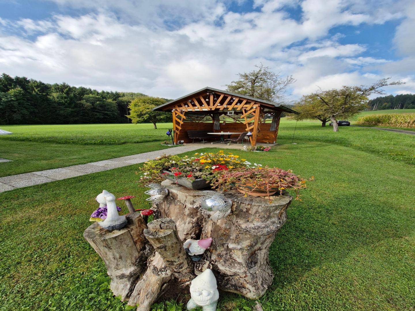 Gemütlicher Holzpavillon mit Sitzgelegenheiten in einem weitläufigen grünen Gartenbereich.