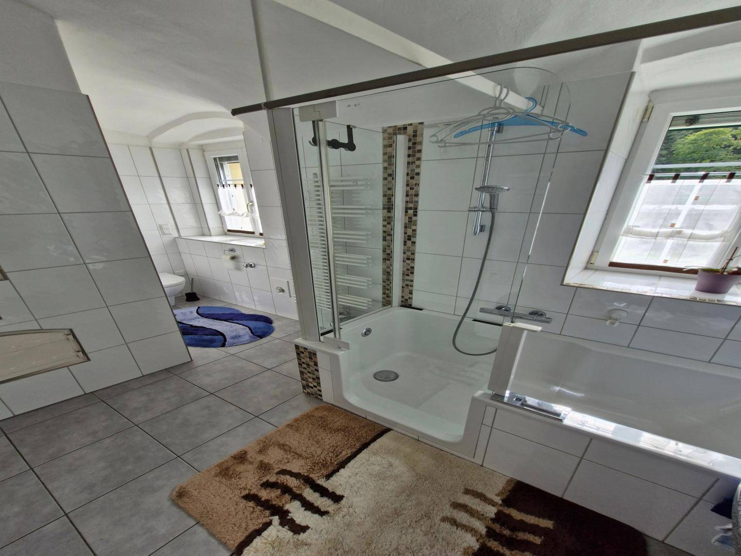 Helles Badezimmer mit begehbarer Dusche, Badewanne und weißen Fliesen, ausgestattet mit einem Fenster.