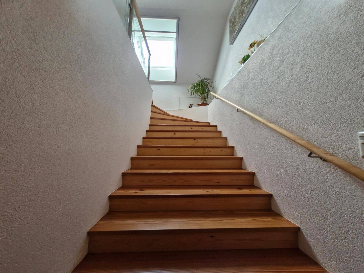 Robuste Holztreppe mit hellem Geländer, die in ein oberes Stockwerk führt.